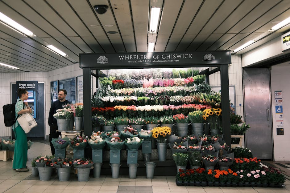 A vibrant flower display at Wheeler of Chiswick situated in an underground station with a variety of freshly cut flowers arranged in metal buckets and wrapped bouquets. The arrangement includes roses,